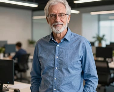A portrait of a senior mobile developer wearing a blue shirt, standing in a modern, open-concept office. Global / Western.