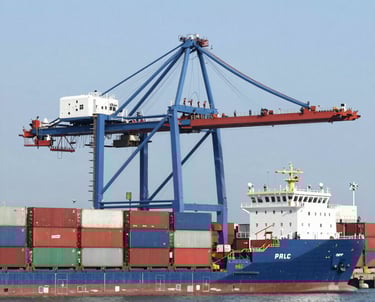 A busy port with colorful shipping containers stacked and cranes loading cargo onto a large vessel under a clear sky.