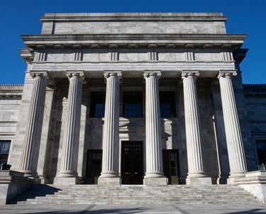 A North American courthouse entrance with grand stone pillars under a clear blue sky. The composition is wide and professional, suggesting stability and justice. The colors are crisp with high contrast, highlighting the Prussian Blue shadows.