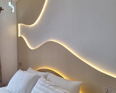 Modern bedroom featuring a minimalist headboard with warm LED wave lighting and white pillows.
