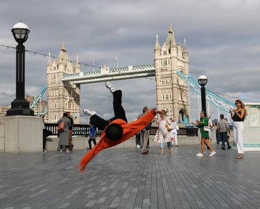YoYo breakdancing with Tower Bridge, London, in the background as passers-by watch.