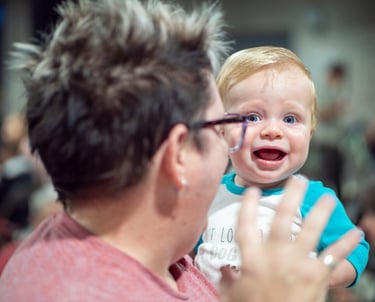 Camera focused on a smiling baby held by an adult
