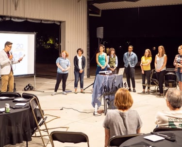CEO presenting by a screen holding a microphone, with the staff lined up nearby