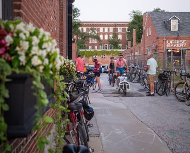 People on bikes riding through an alley with empty bikes propped up on either side
