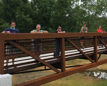 Photo of people standing in a line on a trail bridge smiling at the camera