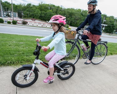 A mother and daughter riding bikes together on a sidewalk