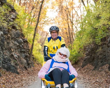 Two smiling people, one sitting in the giving rides bike, and one positioned above them pedaling