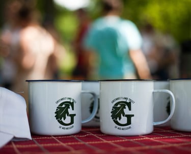 Close up of a bunch of white mugs stamped with the Greenbelt Land Trust logo