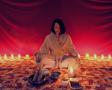 a woman with red background with plenty of candles and ritual tools in a meditative state