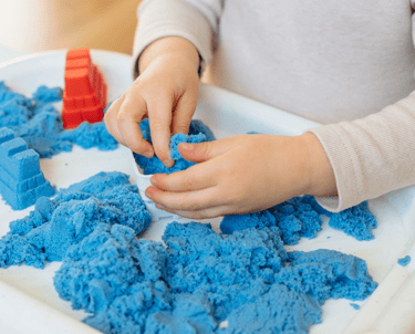 a child's hands holding a toy with blue sand
