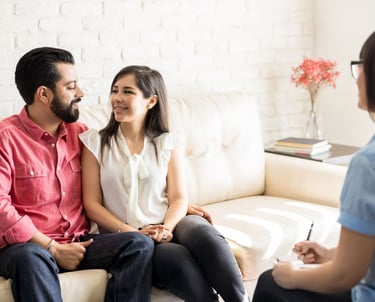Couple sitting close together, smiling at each other during a EFT for couples therapy session with a therapist taking notes