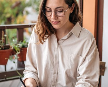 Woman writing in a notebook about her feelings while sitting near a window