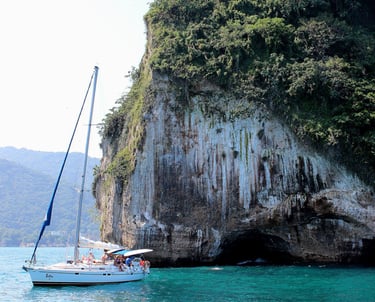 a sailboat in the water near a cliff off the coast of Puerto Vallarta