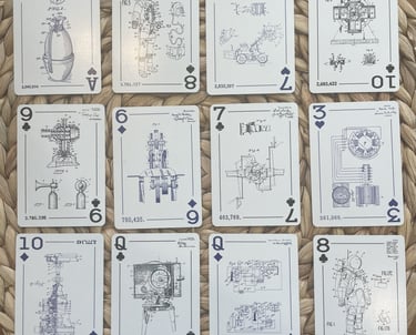 Twelve custom playing cards laid out on a woven surface, each featuring patent drawings on the face