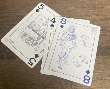 Three custom playing cards face up. The eight of diamonds is on top, showing a space suit drawing