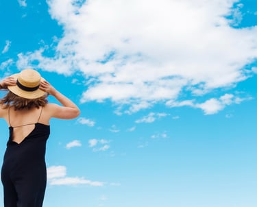 Mulher com chapéu de costas olhando o céu azul