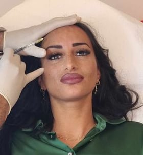 a woman in a green shirt and gloves is getting her eyebrows done