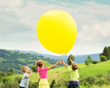two children playing with a large yellow balloon