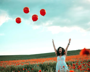 a woman in a white dress is standing in a field with red balloons
