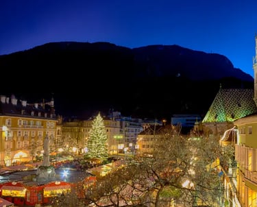 Bolzano Christmas Market at night with the Cathedral of Bolzano and mountains in the background