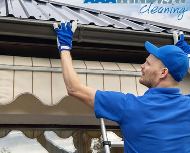 A man in blue cleaning gutters with gloves on