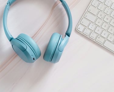 Blue wireless headphones and a white keyboard on a clean desk, symbolizing online learning, language