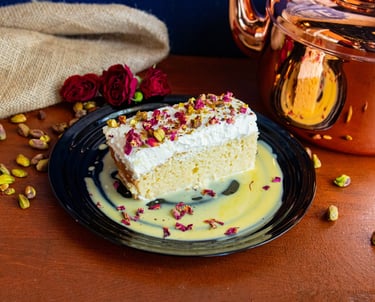 Indian Fusion Dessert Kulfi Tres Leches on a plate with a chai bronze kettle and roses and pistachio