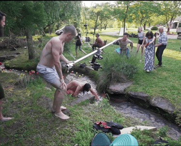 a man is holding a camera rig to film a music video outdoors in the grass