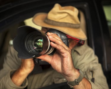 A private investigator takes surveillance photos with a professional DSLR camera from a car.