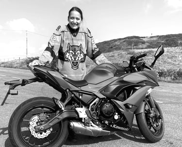 A young rider called Becky stood behind her motorcycle in a countryside landscape