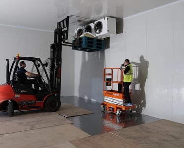 Forklift lifting a large industrial evaporator inside a freezer room during installation process