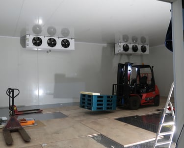 Team installing an evaporator unit with the help of a forklift inside a commercial cold storage faci