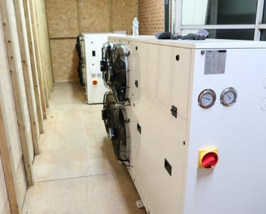 Two large industrial condensers in a commercial freezer room, with one serving as a backup spare uni