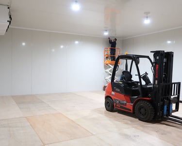 Scissor lift positioned inside a large industrial freezer room, used for instaling of high-mounted