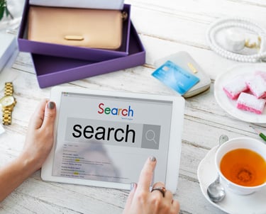 Tablet con la palabra search en pantalla, rodeada de objetos cotidianos como taza de té y cuaderno