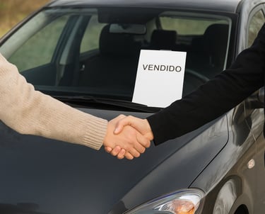 Duas pessoas apertando as mãos em frente a um carro com placa “Vendido” no para-brisa.