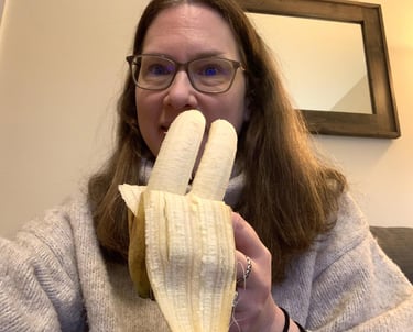 a woman in glasses and a sweater is holding a banana peeler
