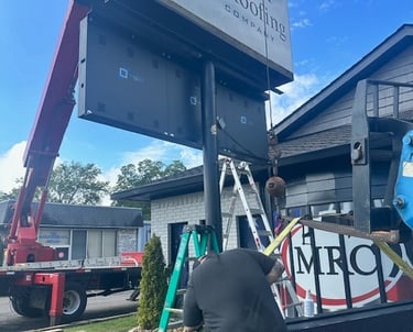 A commercial signage technician installs a digital LED display for Miller Roofing Company using a crane truck.