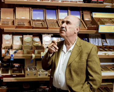 Un homme debout en costume et cravate avec à la main un cigare
