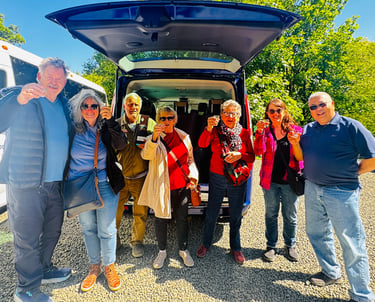 a group of people standing around a van smiling at the camera with drinks in their hands