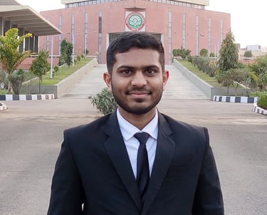 A man in a black suit standing in front of a modern building with a green and red logo. The well-maintained path leading up t