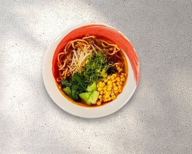Shoyu ramen bowl with wavy noodles, sweet corn, bok choy, and scallions on a grey textured surface.
