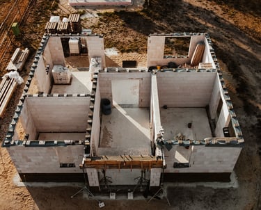 Luftaufnahme einen Rohbaus mit bereits errichteten Mauern und offenen Grundriss auf einer Baustelle 
