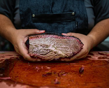 pitmaster holding a smoked brisket over a cutting board
