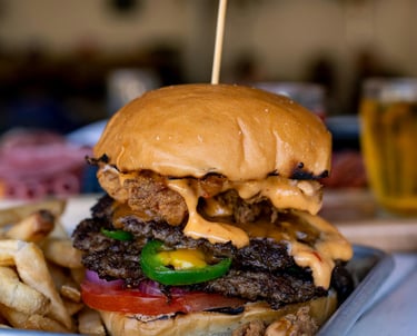 cheeseburger with tomato, onion, jalapeno, and fries on the side, on metal plate