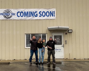 Premier Tire shop coming soon banner on building with staff standing outside.