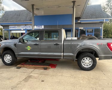 Gray Ford F-150 truck lifted on a hydraulic jack for tire service at an automotive repair shop.