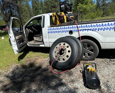 Mobile tire service truck inflating semi-truck tires with a portable air compressor in a rural area.