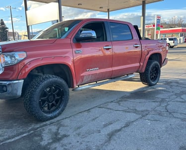 A lifted red Toyota Tundra 4x4 pickup truck with black off-road wheels parked at a gas station.