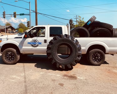 White Premier Tire service truck hauling oversized tractor and commercial truck tires outdoors.